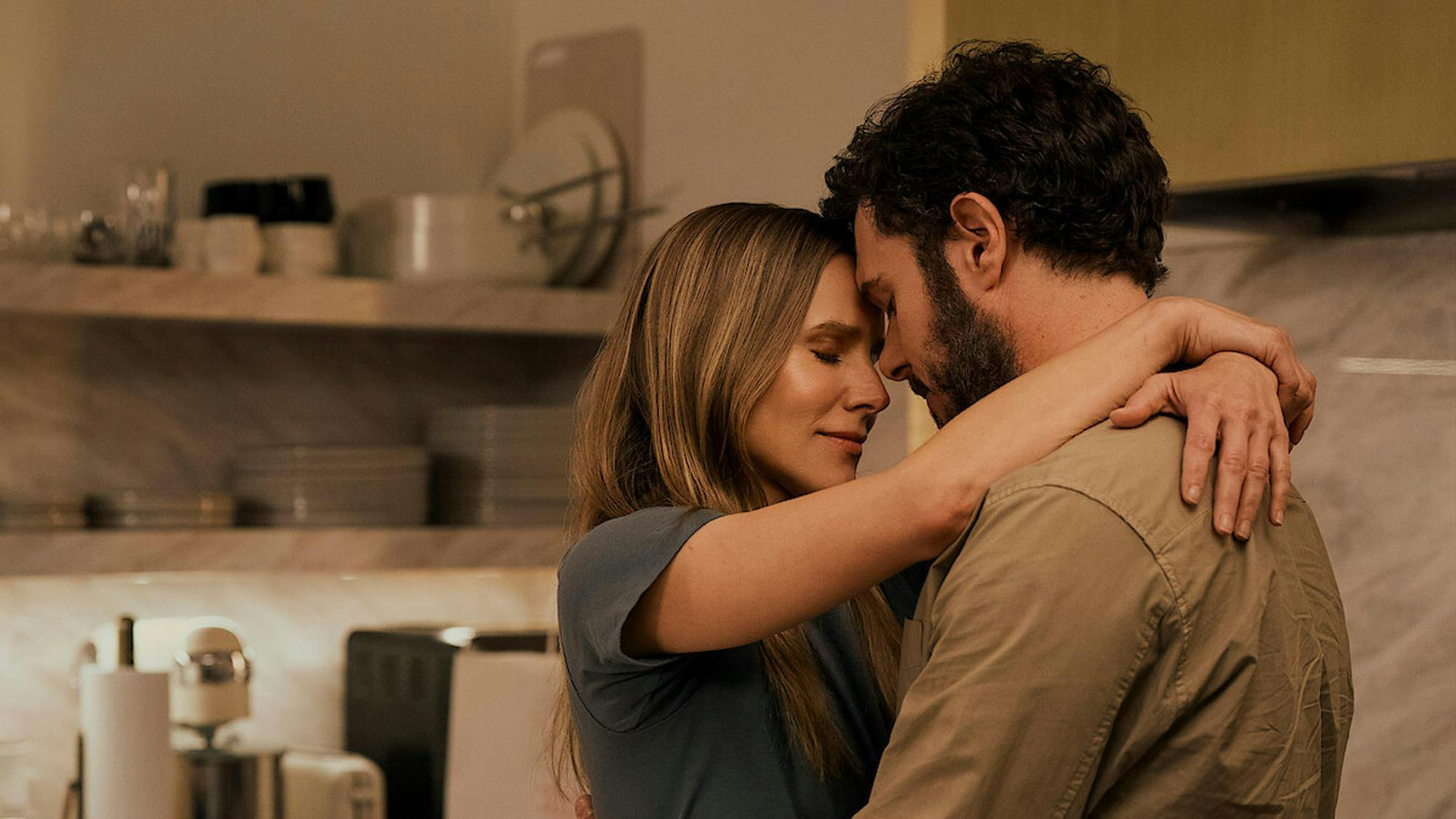 Frame from "Nobody Wants This" showing a man and a woman, Adam Brody and Kristen Bell, embracing with their foreheads touching and eyes closed.