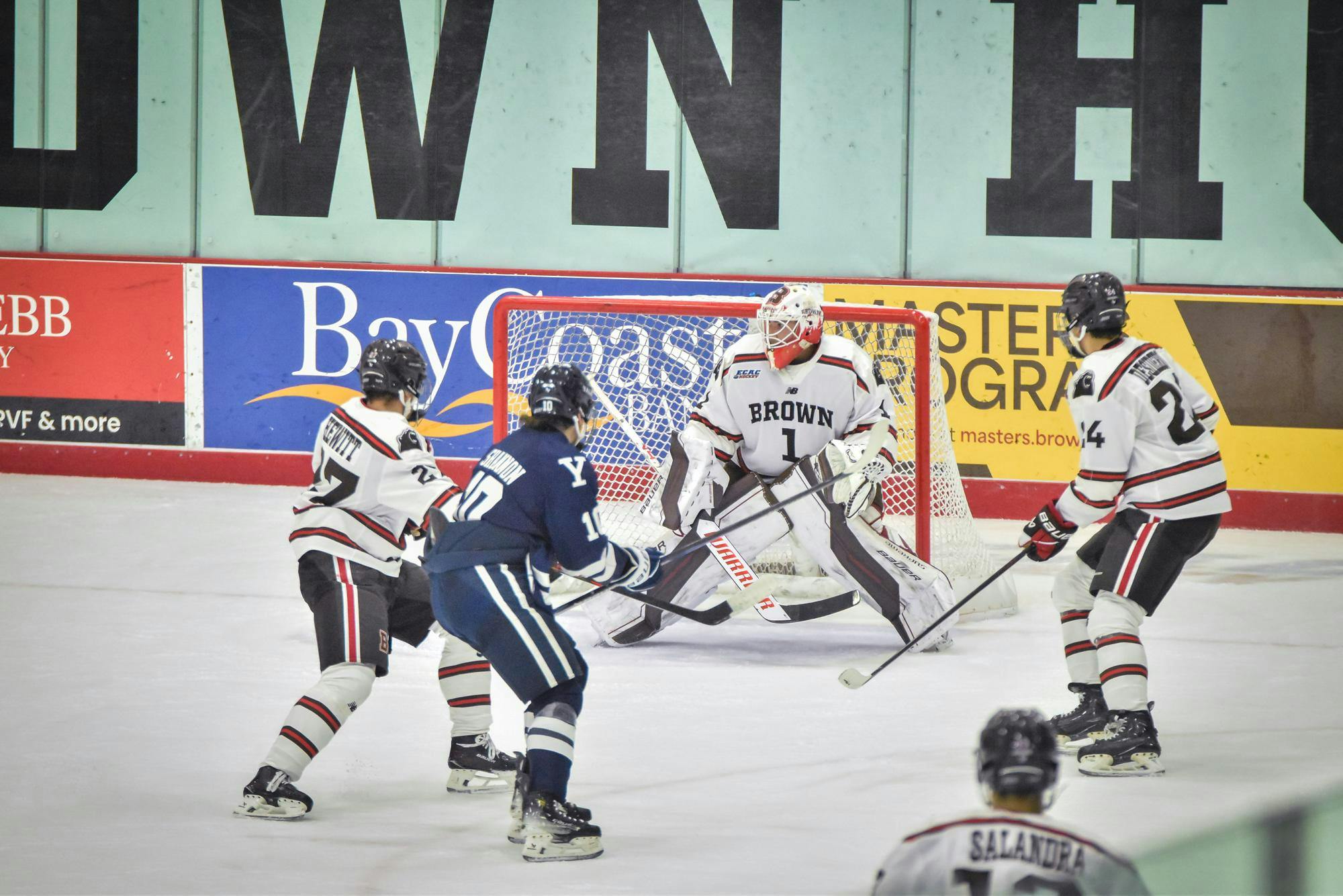 Photo of three hockey players surrounding a goalie on the ice.