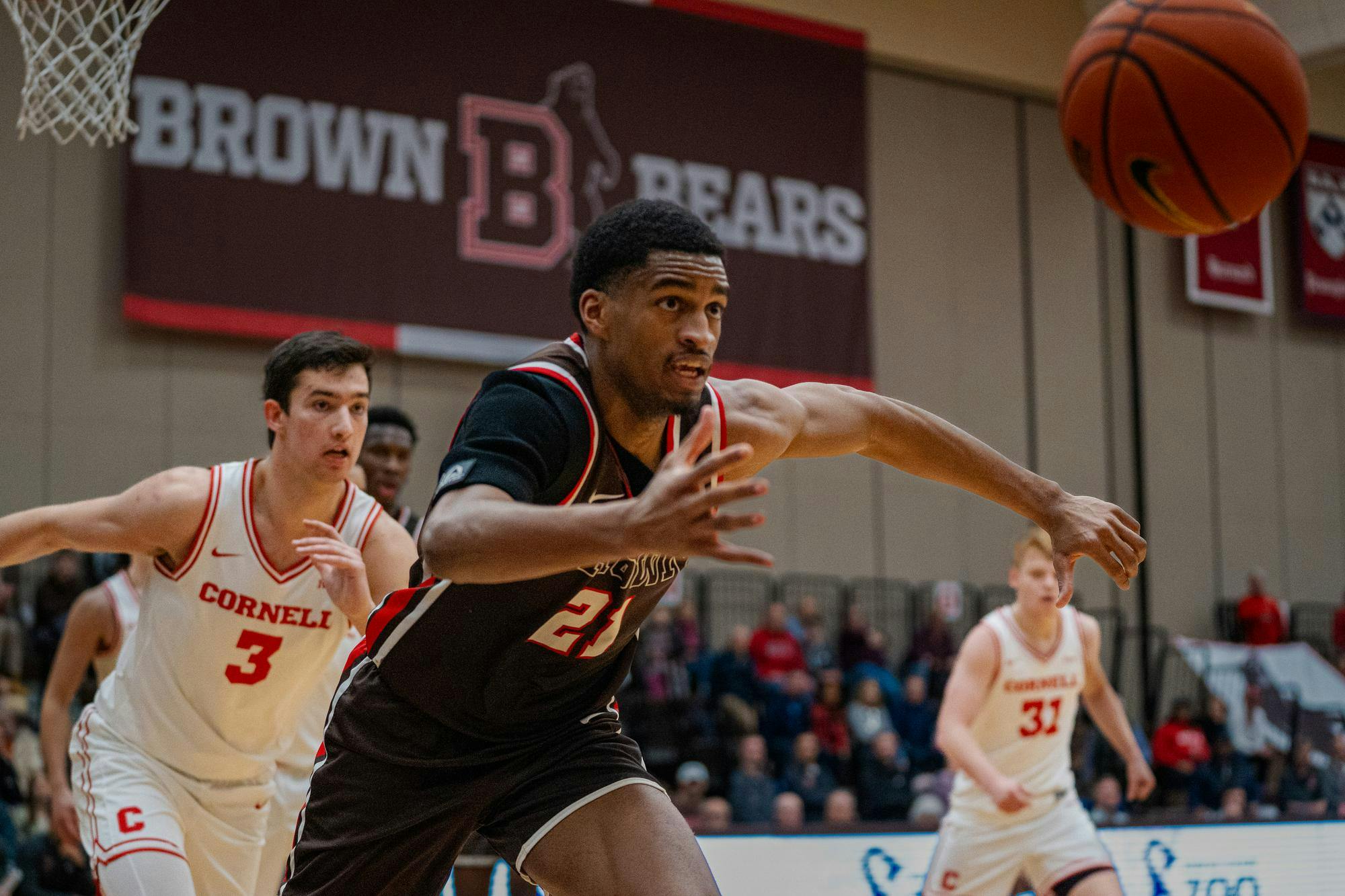 Brown Basketball player Aaron Cooley chasing a ball versus a Cornell player.