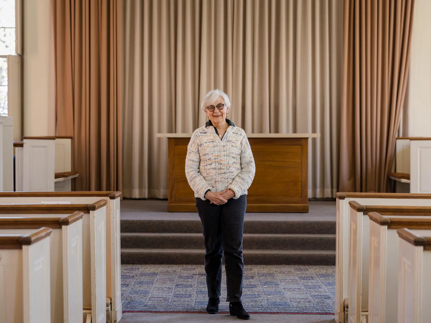 Janet Cooper Nelson stands in the front of the Manning Chapel, wearing a pale sweater and dark pants.