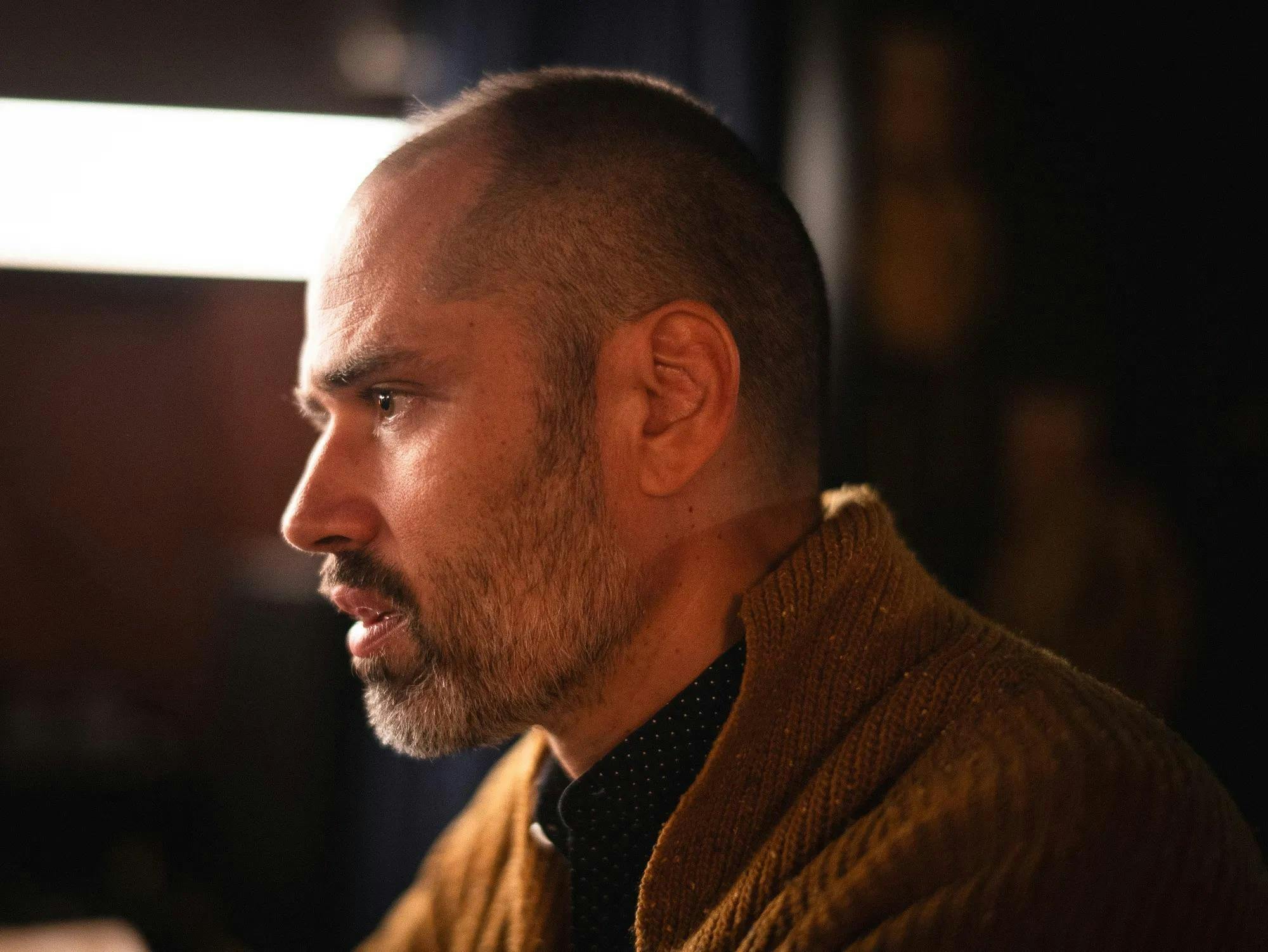 Photo of William Brittelle wearing a blue polka dot shirt and orange sweater. 