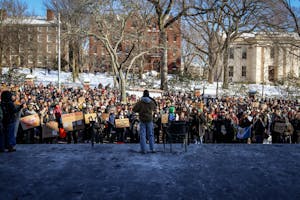 A man speaks to a large crowd on the steps of Brown University’s John D. Rockefeller Jr. Library. Many people within the crowd hold signs and wear masks.  