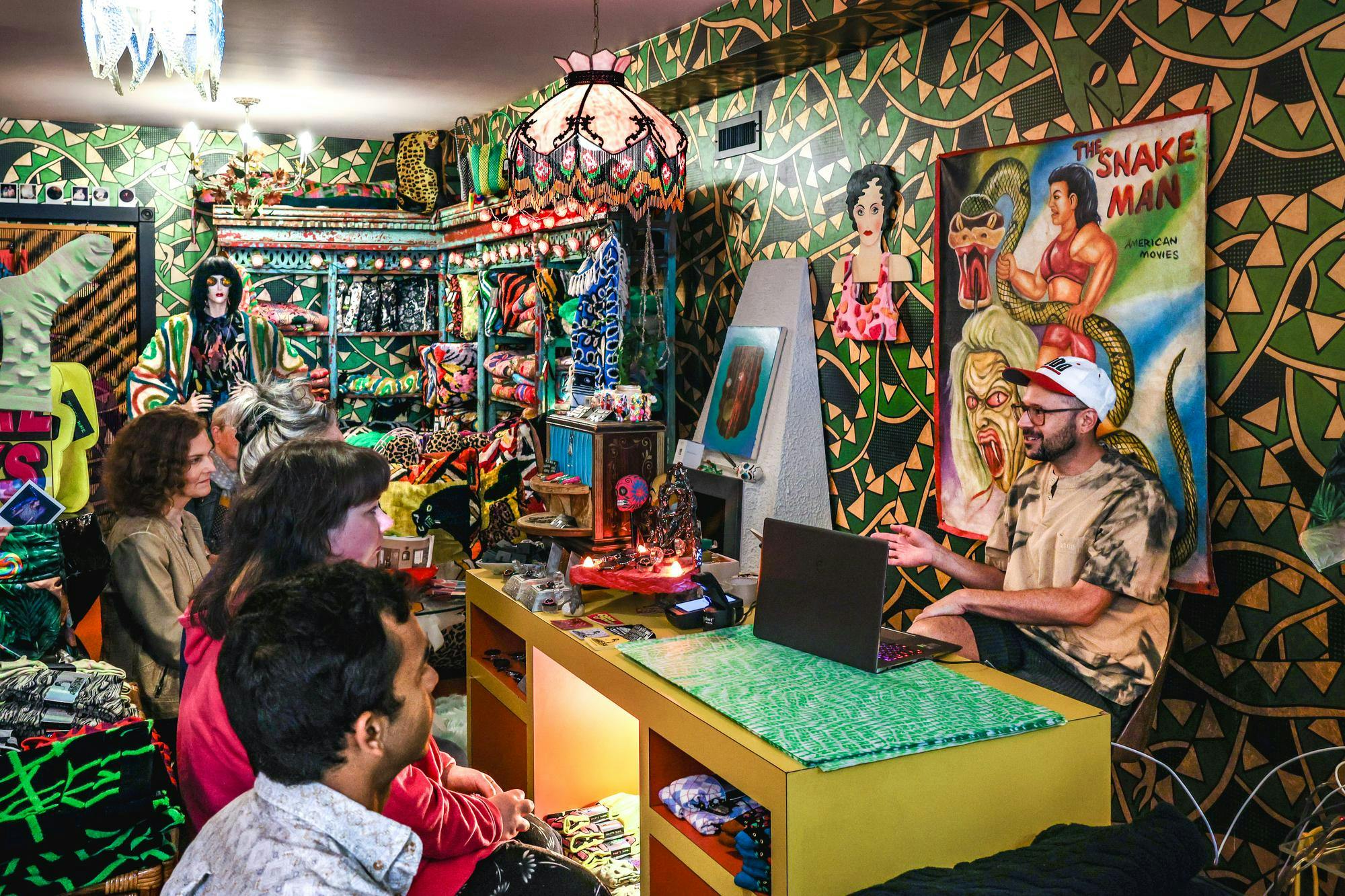 An artist talking to a group of people in a room filled with crafts.