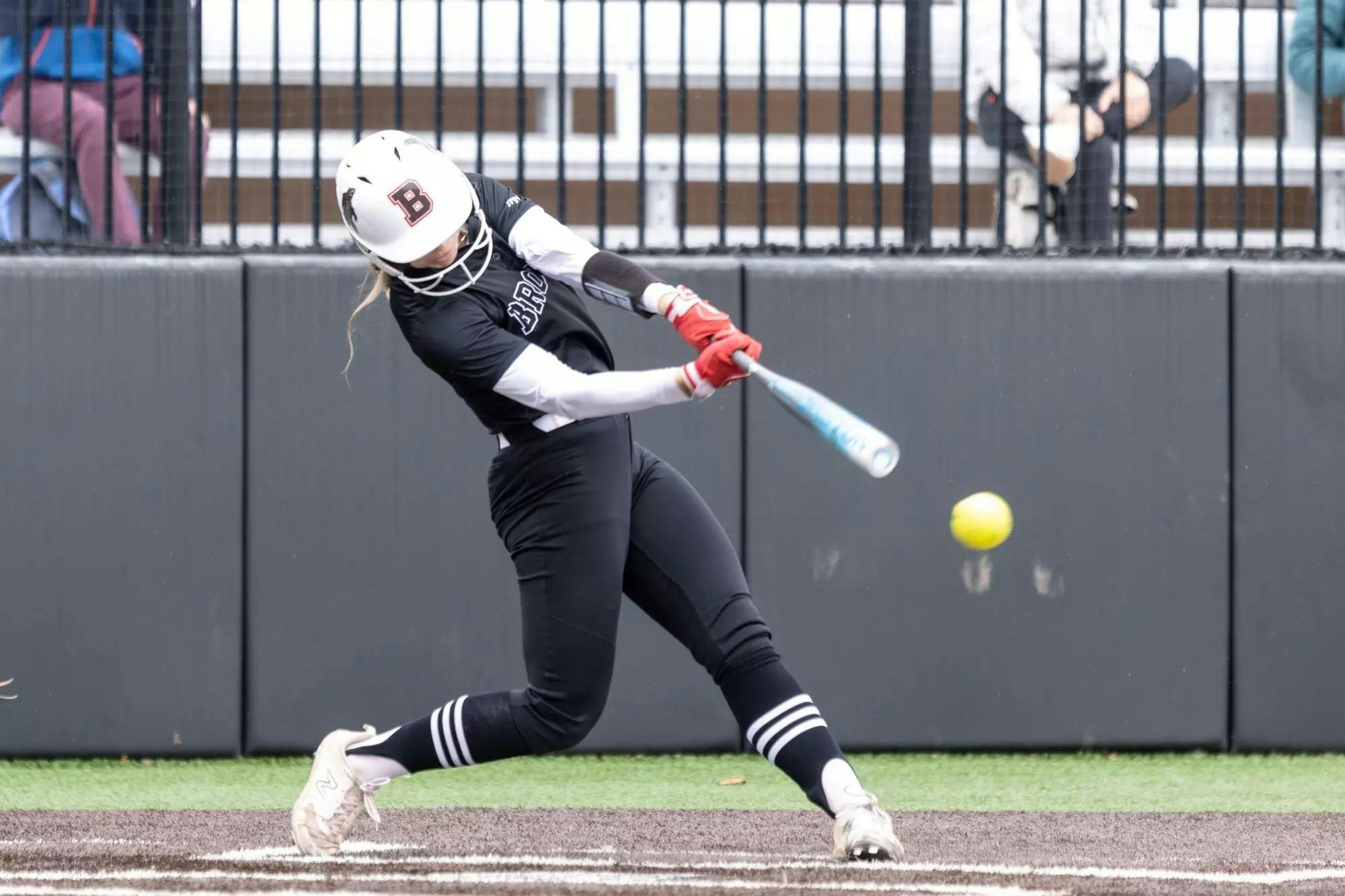 A Brown women's softball player swings at an incoming pitch. 