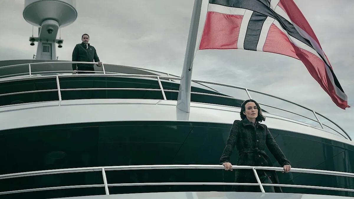 Photo of a woman looking over the railing of a boat with a man peering over her from the floor above. 