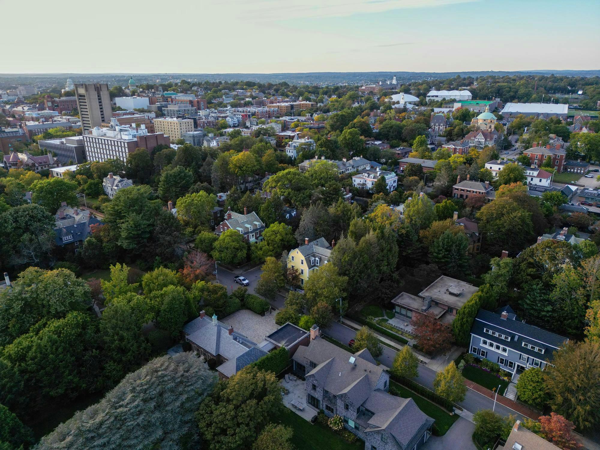 Aerial photo of College Hill viewed from Fox Point, with houses and University buildings scattered among green trees. 