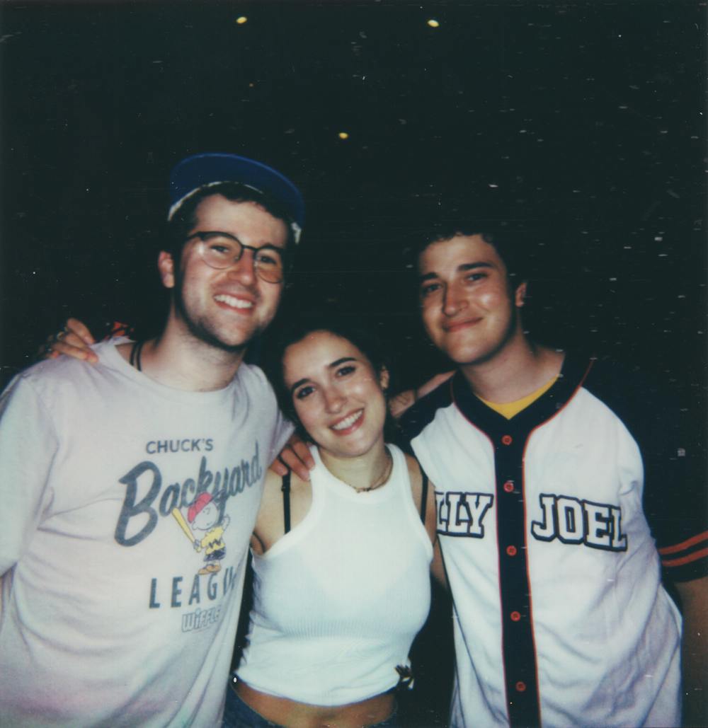 A Polaroid photo of two men on either side of a woman. All three smile at the camera. 