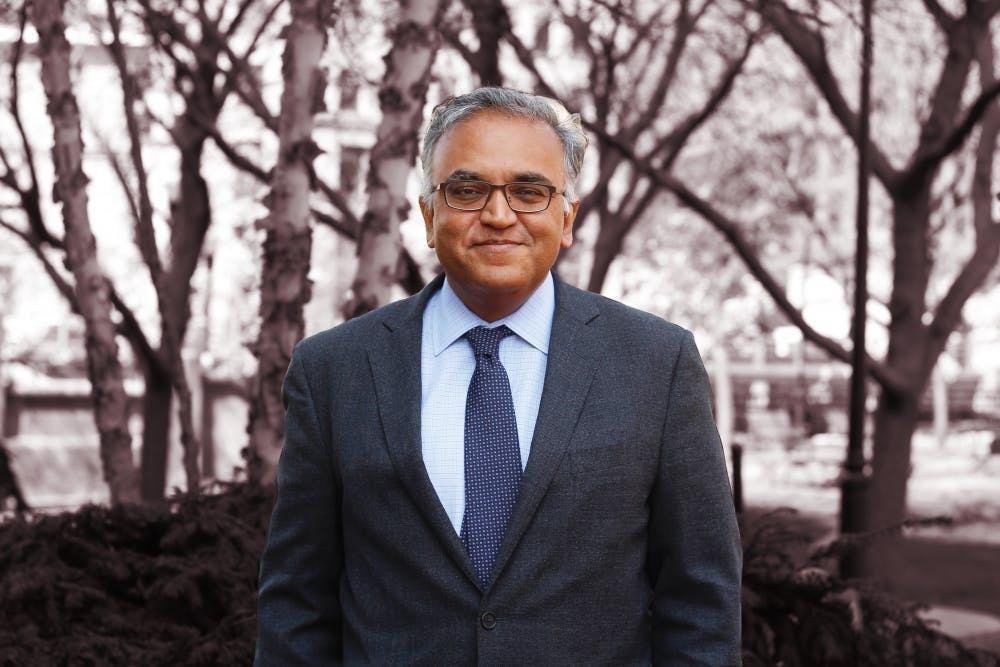 A headshot of Ashish Jha wearing a suit with a blue tie in front of some trees. 