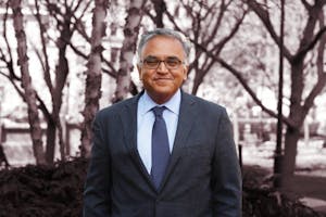 A headshot of Ashish Jha wearing a suit with a blue tie in front of some trees. 