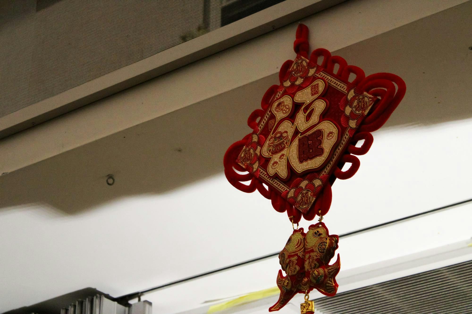 Photo of the Chinese symbol for prosperity written in gold on a red diamond with traditional Chinese knots around the diamond and two fish hanging below with gold detailing.