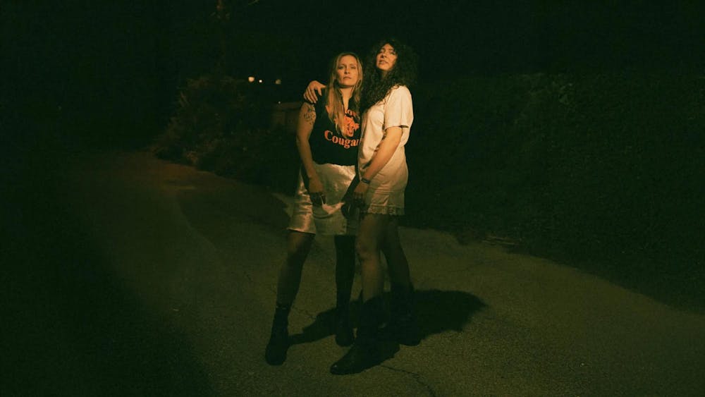 Sisters Natalie and Meegan Closner pose for a nighttime film photo, flash illuminating their faces. Natalie, on the right, puts her arm around Meegan.

