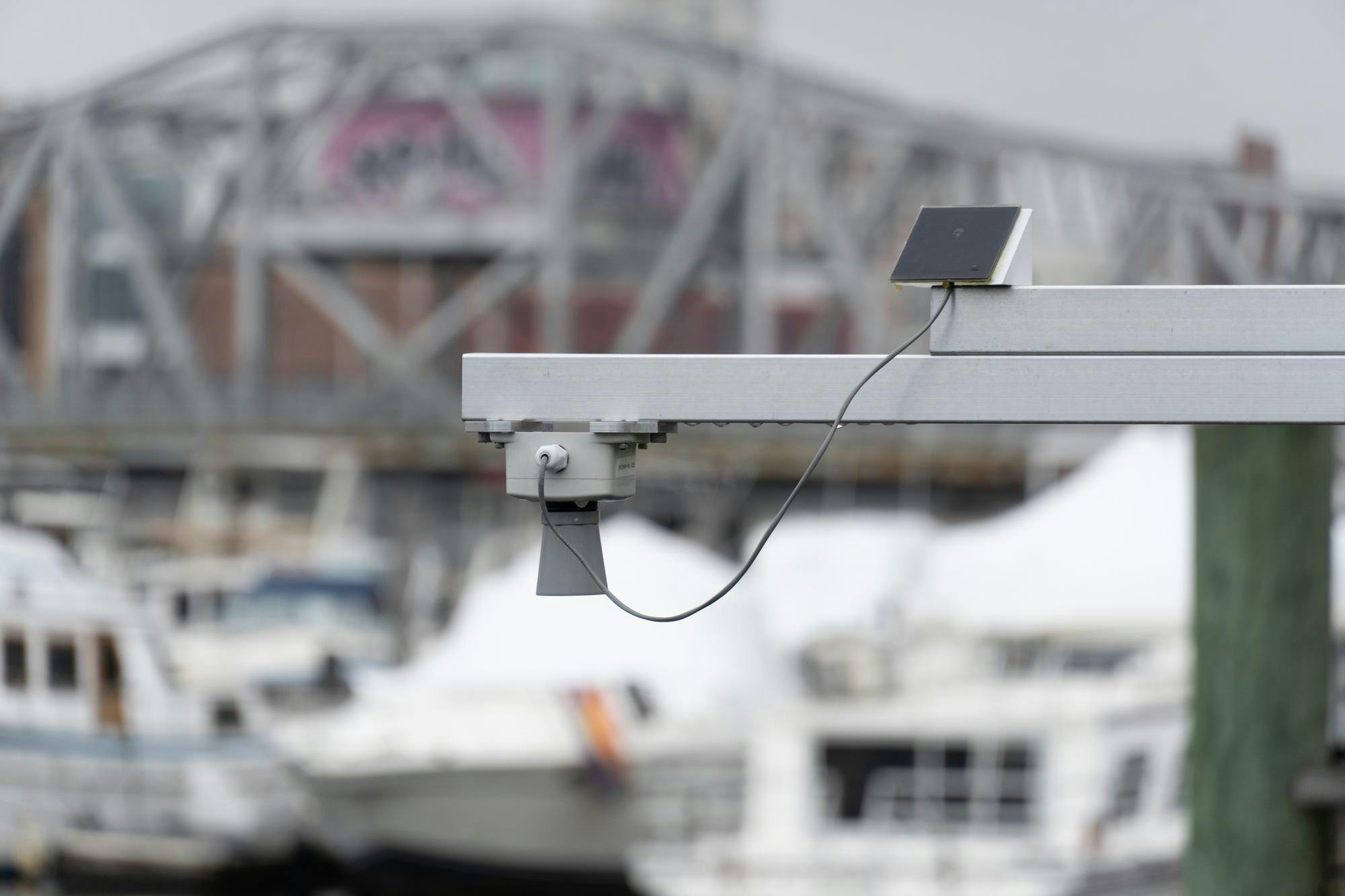 An image of an air sensor on a gray platform with a blurred dock of ships and a bridge in the background. 