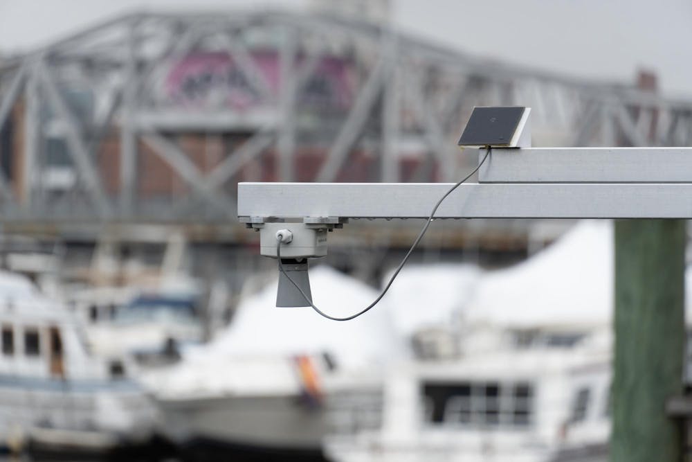 An image of an air sensor on a gray platform with a blurred dock of ships and a bridge in the background. 