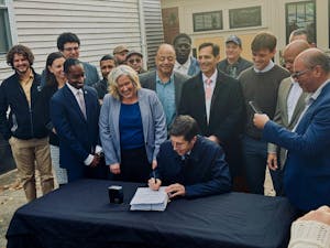 Providence Mayor Brett Smiley sits at a table surrounded by over a dozen people while signing the Comprehensive Plan on Friday.