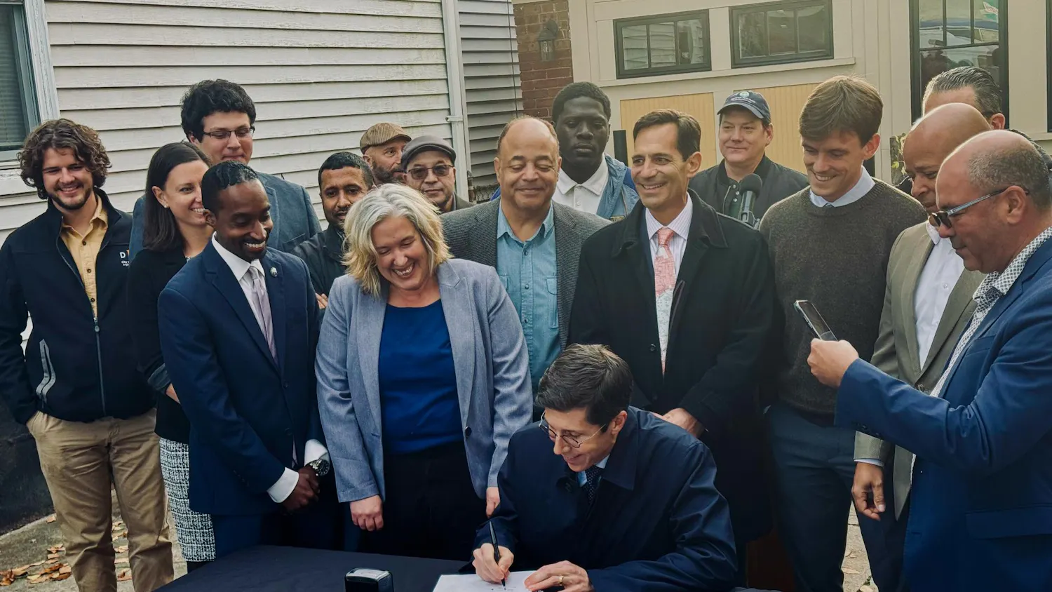 Providence Mayor Brett Smiley sits at a table surrounded by over a dozen people while signing the Comprehensive Plan on Friday.