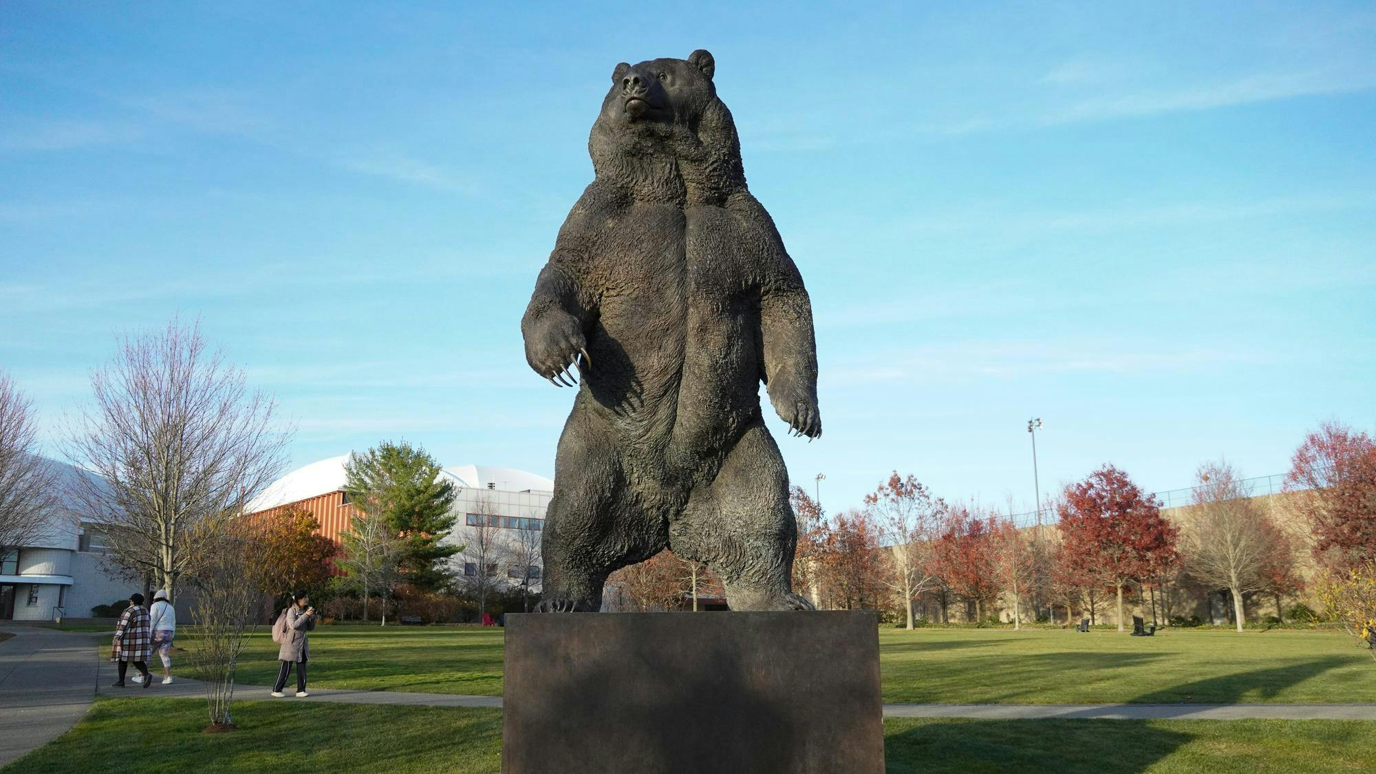 Photo of a statue of a bear standing on its hind legs looking towards the left in the middle of a field with paths and trees without leaves.