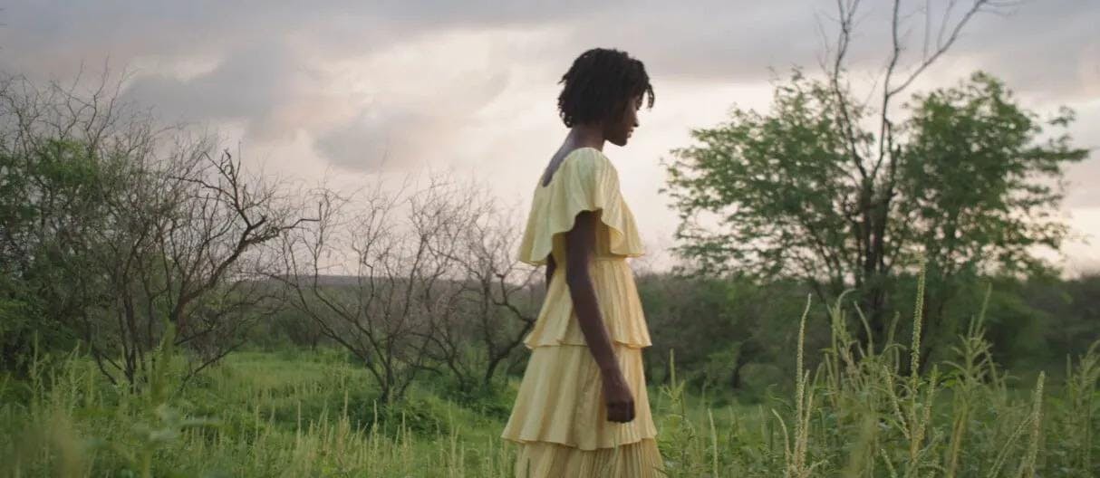A still from the short film Pirinha depicting a woman in a yellow dress standing in a field.