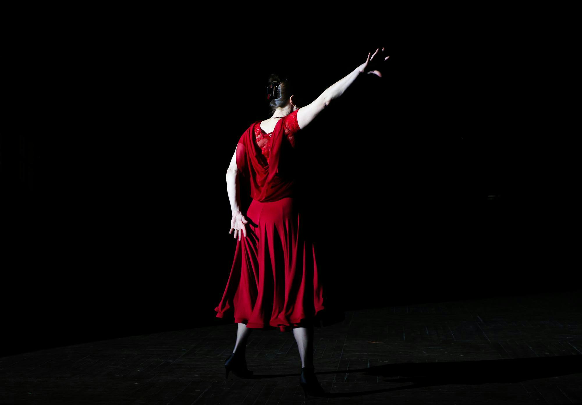 A woman in a red dress from behind, framed by a black background.
