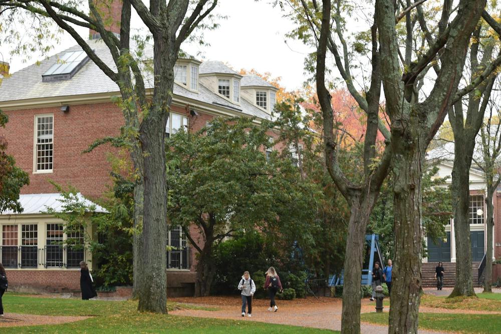 A photo of Patriot Court in early fall. Students are walking along the paths and the leaves on some trees are turning orange. 