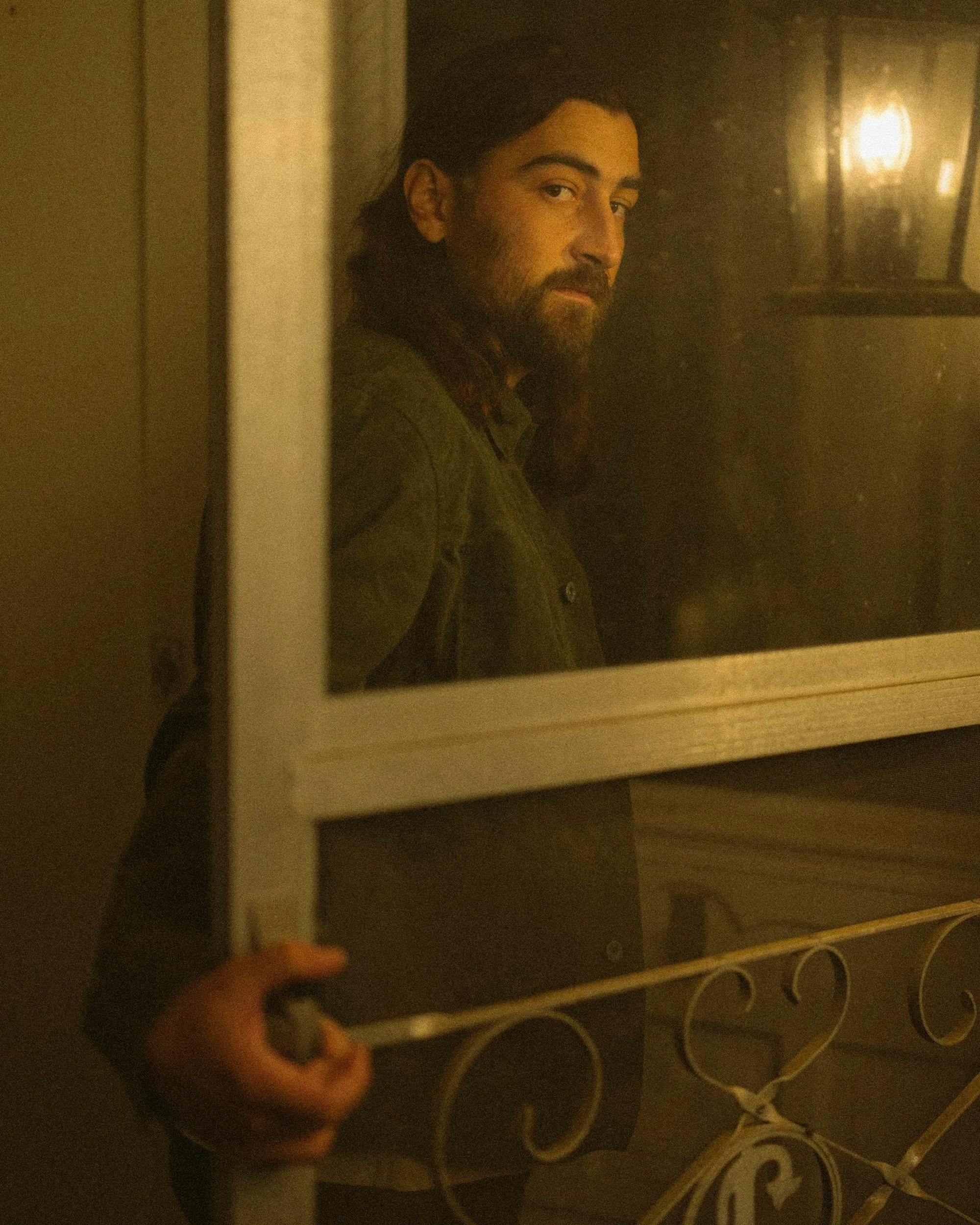 Image of Noah Kahan looking back at the camera while holding open a door.