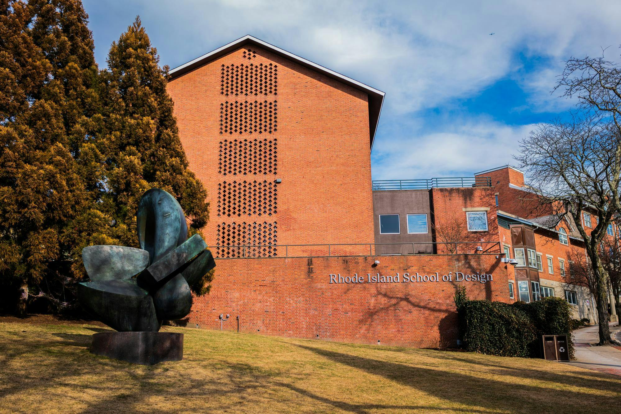 A view of a Rhode Island School of Design building on Benefit Street. In front of the brick building, there is a green statue and a large tree.