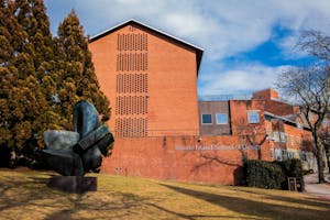 A view of a Rhode Island School of Design building on Benefit Street. In front of the brick building, there is a green statue and a large tree.