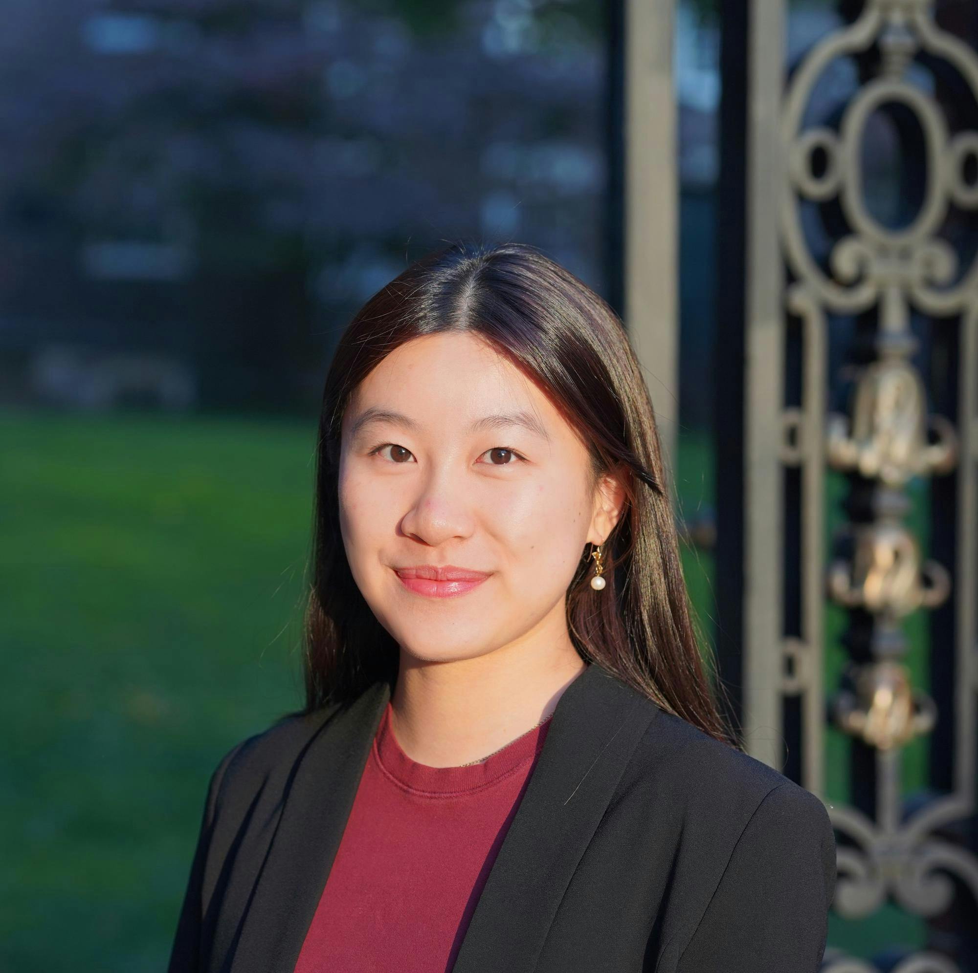A headshot of Clara Tandar outside on a sunny day wearing a red shirt and black blazer. 