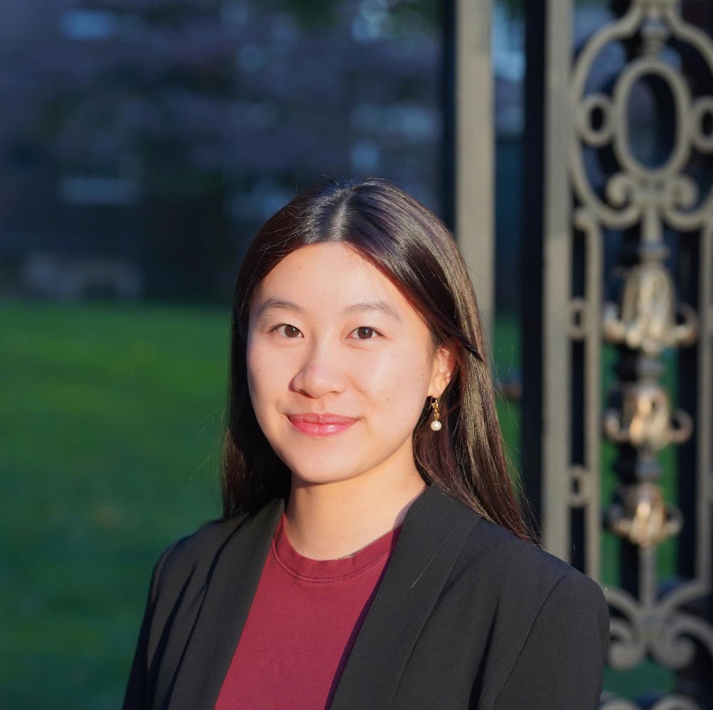 A headshot of Clara Tandar outside on a sunny day wearing a red shirt and black blazer. 