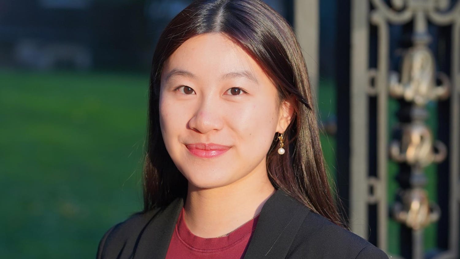 A headshot of Clara Tandar outside on a sunny day wearing a red shirt and black blazer.