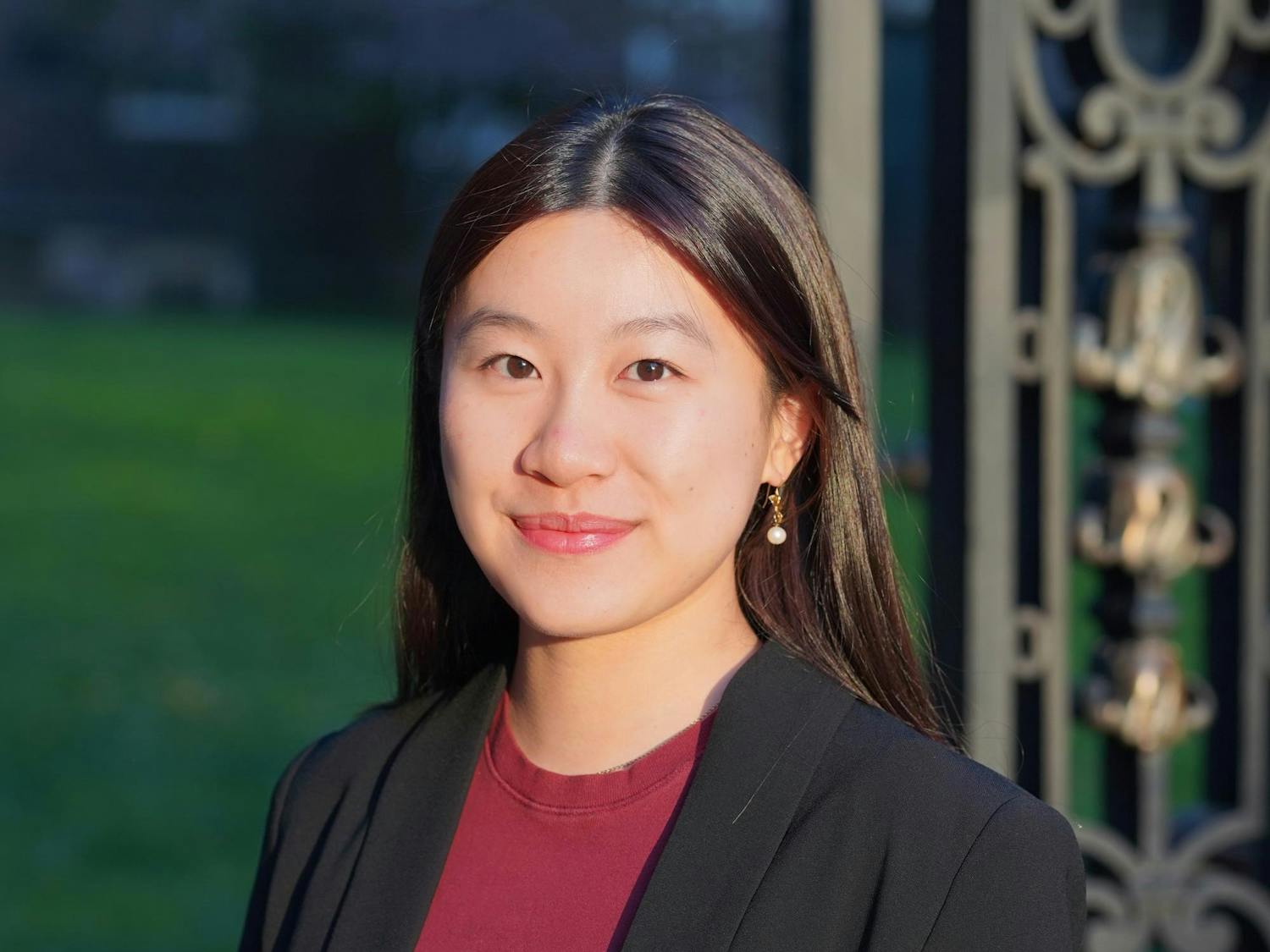 A headshot of Clara Tandar outside on a sunny day wearing a red shirt and black blazer.