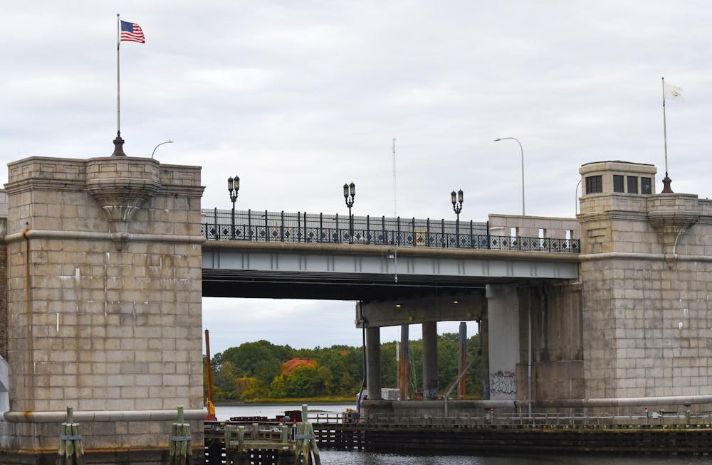 Concrete and metal bridge with three black lampposts lined throughout. Brick columns are on the sides of the bridge with an American flag on a pole waving on the left column.