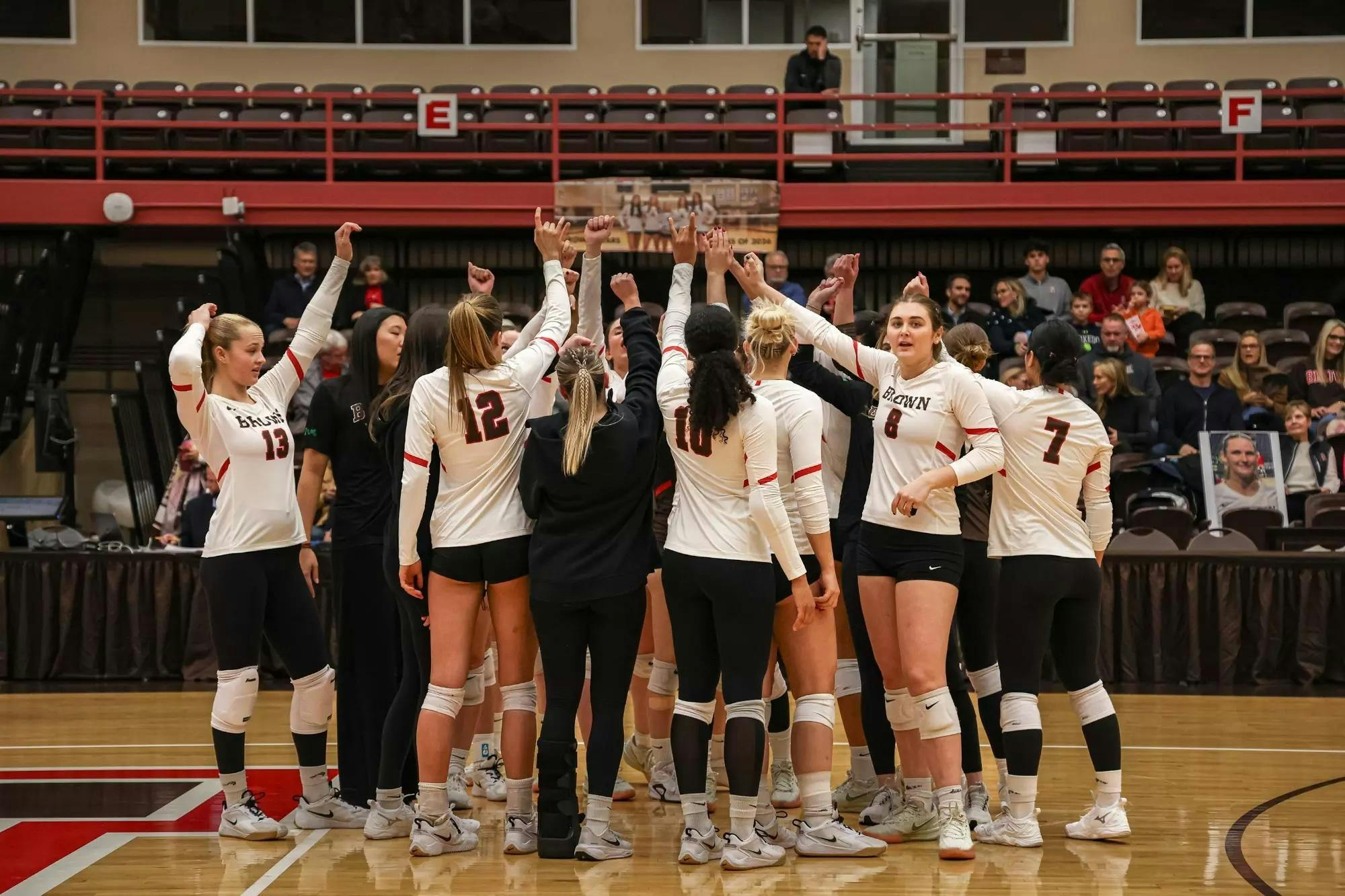 Brown Univeristy's Women's Volleyball Team huddled in a group with their fists in the air. 