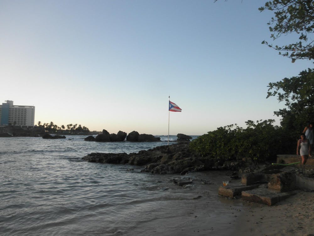 Photo of the beach during sunset with a Puerto Rican flag on a pole on a rock. 