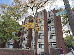 Photo of Grad Center. The photo shows a brick building with a wall of windows in the background and vibrant trees in the foreground. 