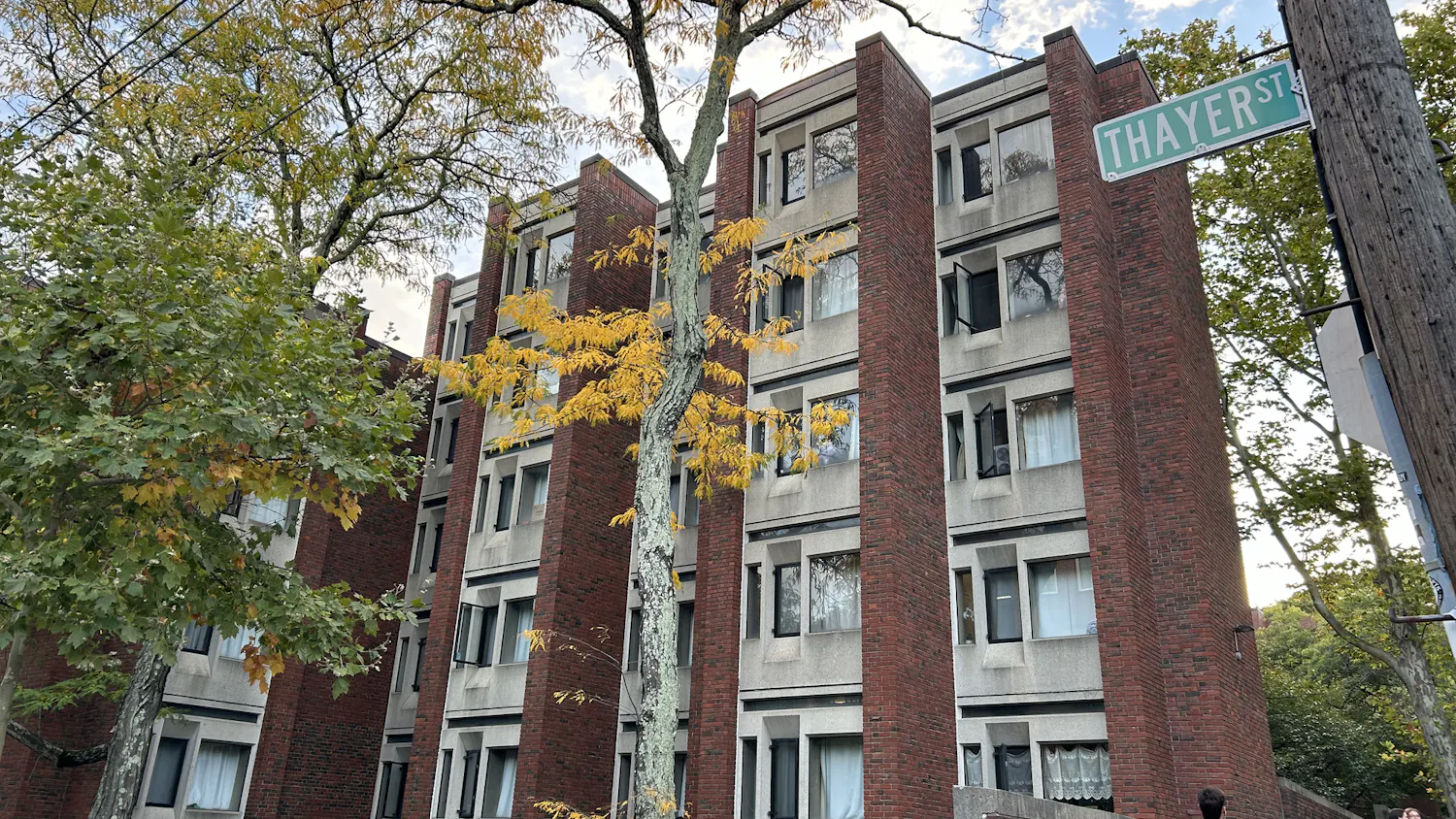 Photo of Grad Center. The photo shows a brick building with a wall of windows in the background and vibrant trees in the foreground.