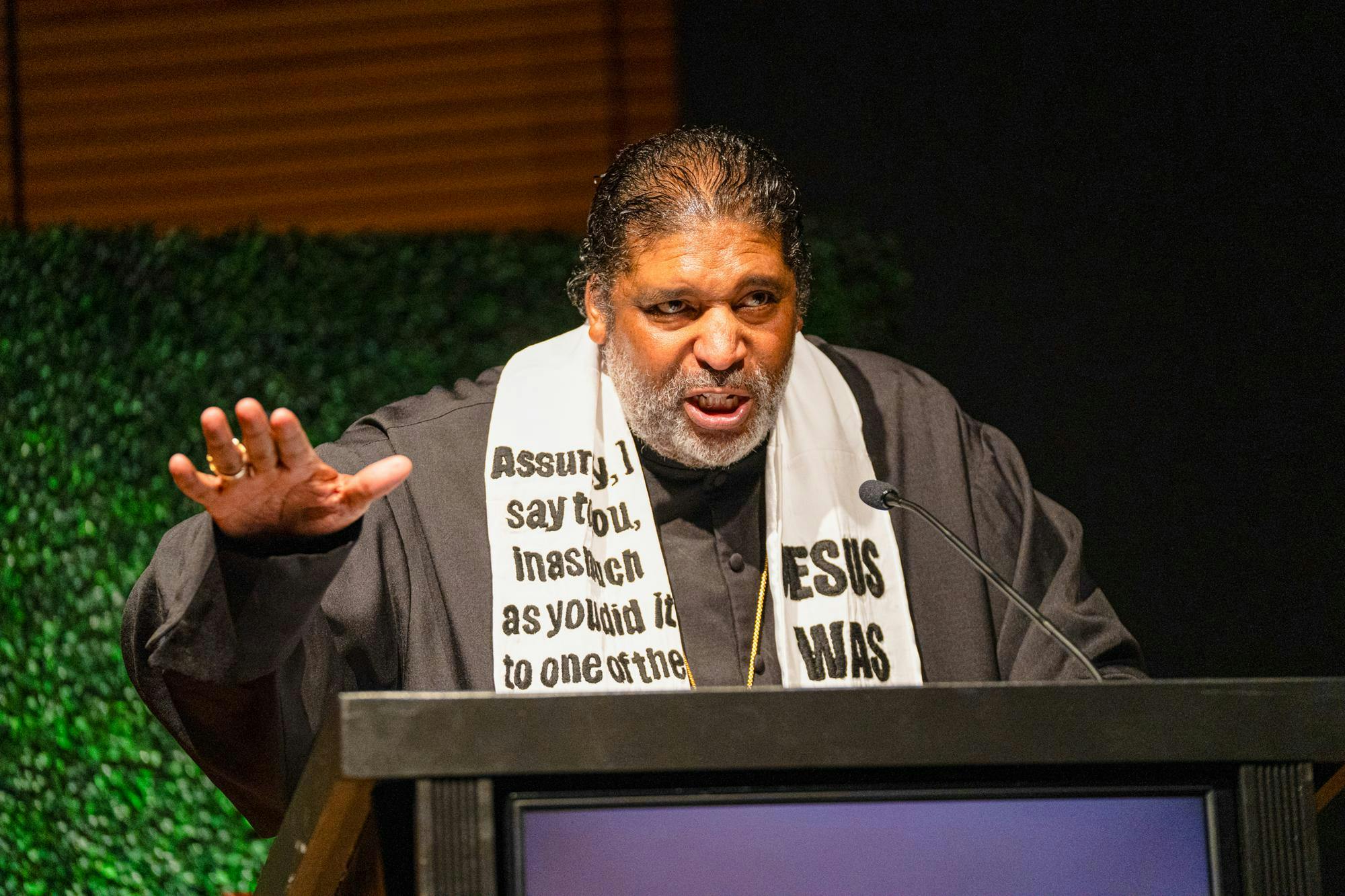 The picture shows Reverend William J. Barber II behind a black podium. He is wearing a black robe with a white stole. 