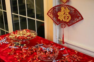 Photo of a Chinese character for prosperity in yellow on top of a red piece of felt with cutouts. A table with a red tablecloth has assorted Chinese candies in red, white, and yellow wrapping on it.

