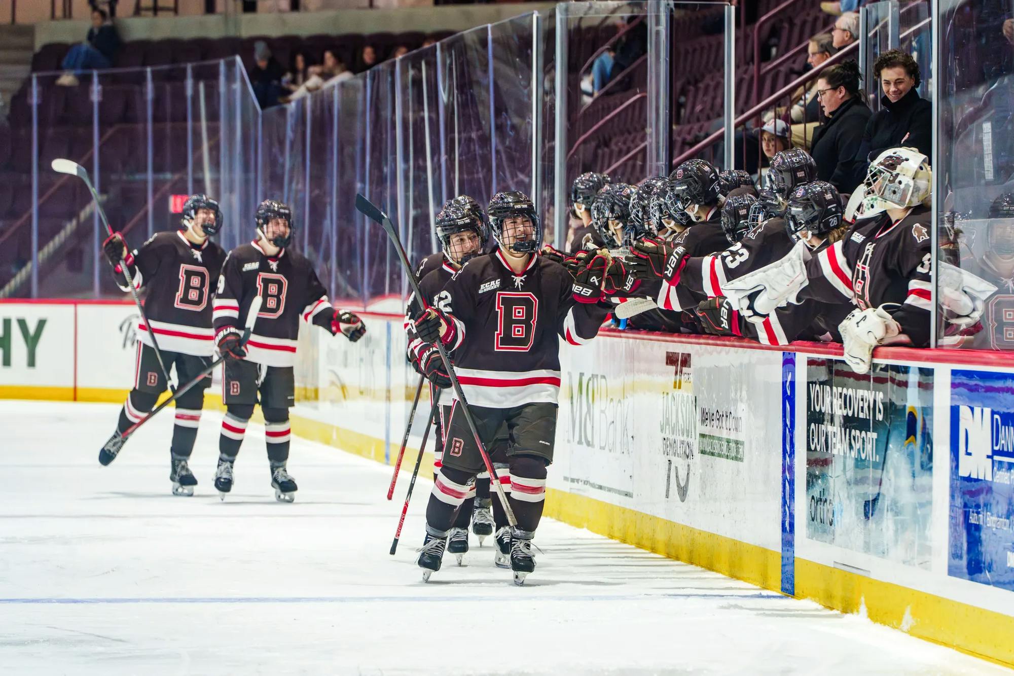 Photo of members of the Brown Women’s Hockey team high-fiving their teammates on an ice rink.