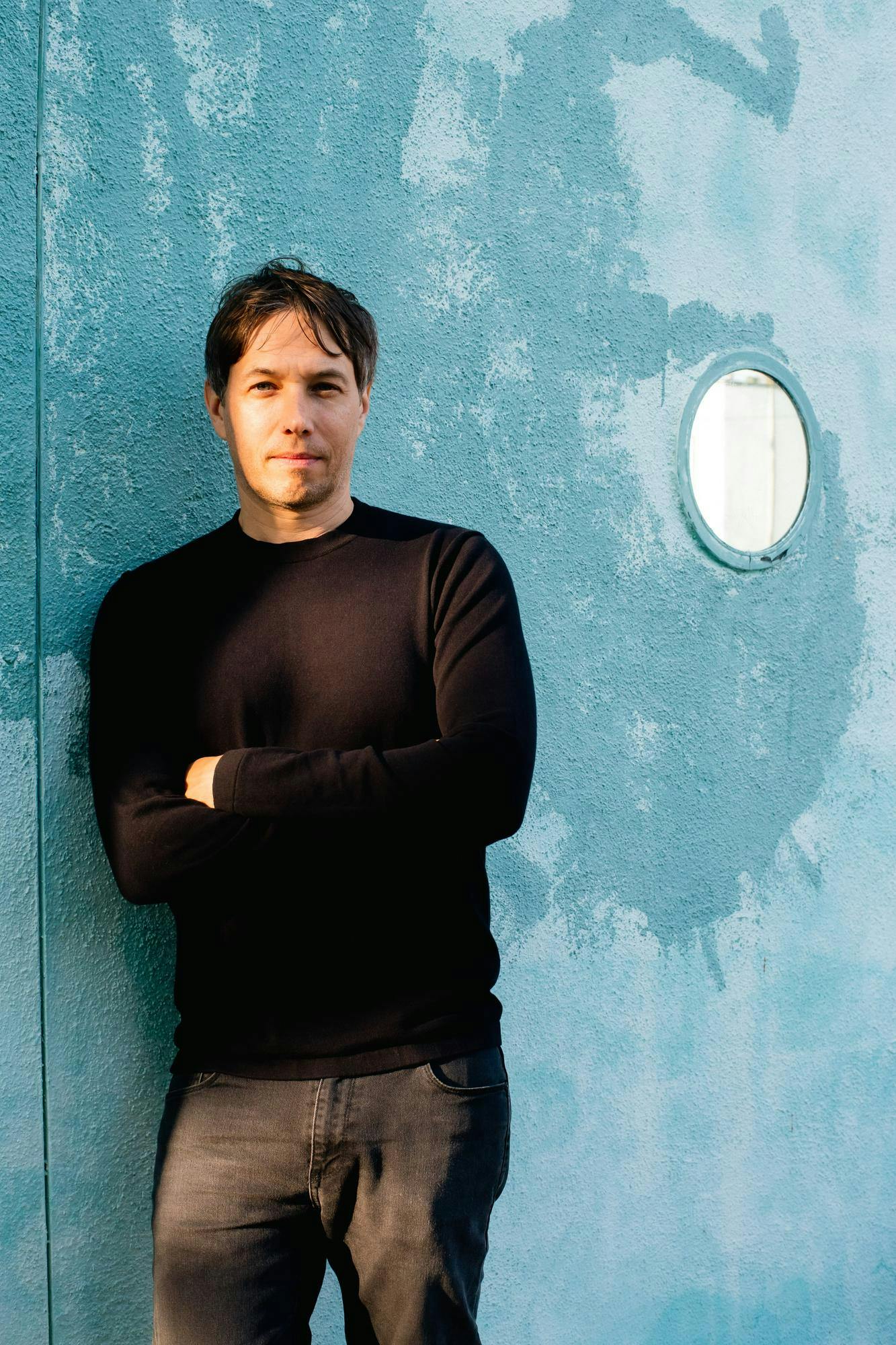 Sean Baker poses wistfully before a cyan wall. 