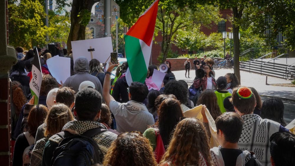 Photo of a group of students marching on the sidewalk with signs and a flag.
