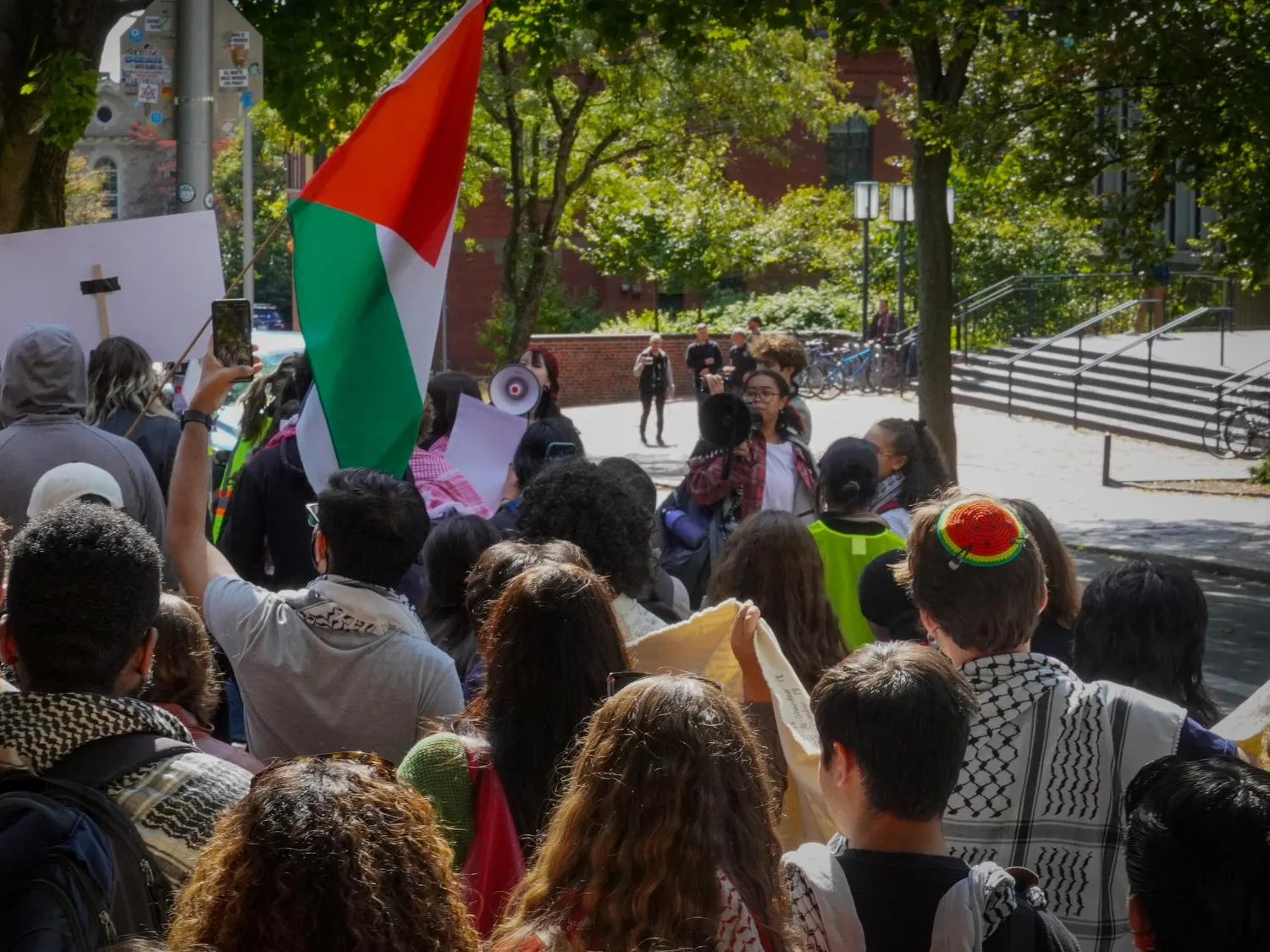Photo of a group of students marching on the sidewalk with signs and a flag.