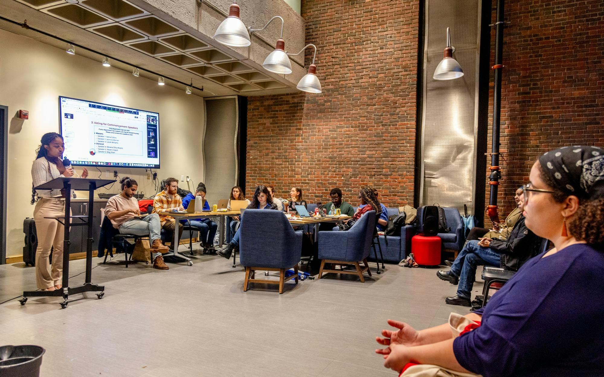 Photo of the Graduate Student Council meeting in April, where a group of students sit around a speaker and TV.
