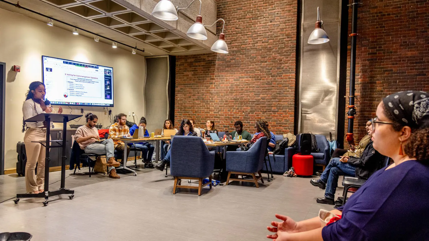 Photo of the Graduate Student Council meeting in April, where a group of students sit around a speaker and TV.