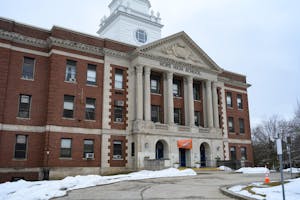 Photo of Hope High School in perspective, featuring the red brick facade, entrance area with white columns, and a driveway in the front. 