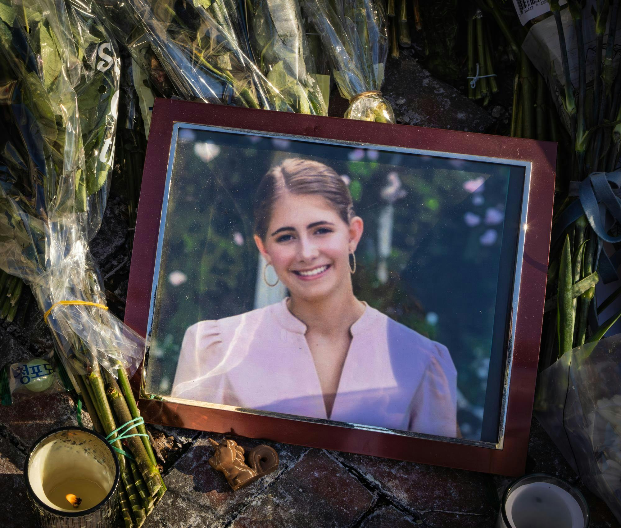 A picture frame of a smiling girl sits on top of bouquets of flowers. 