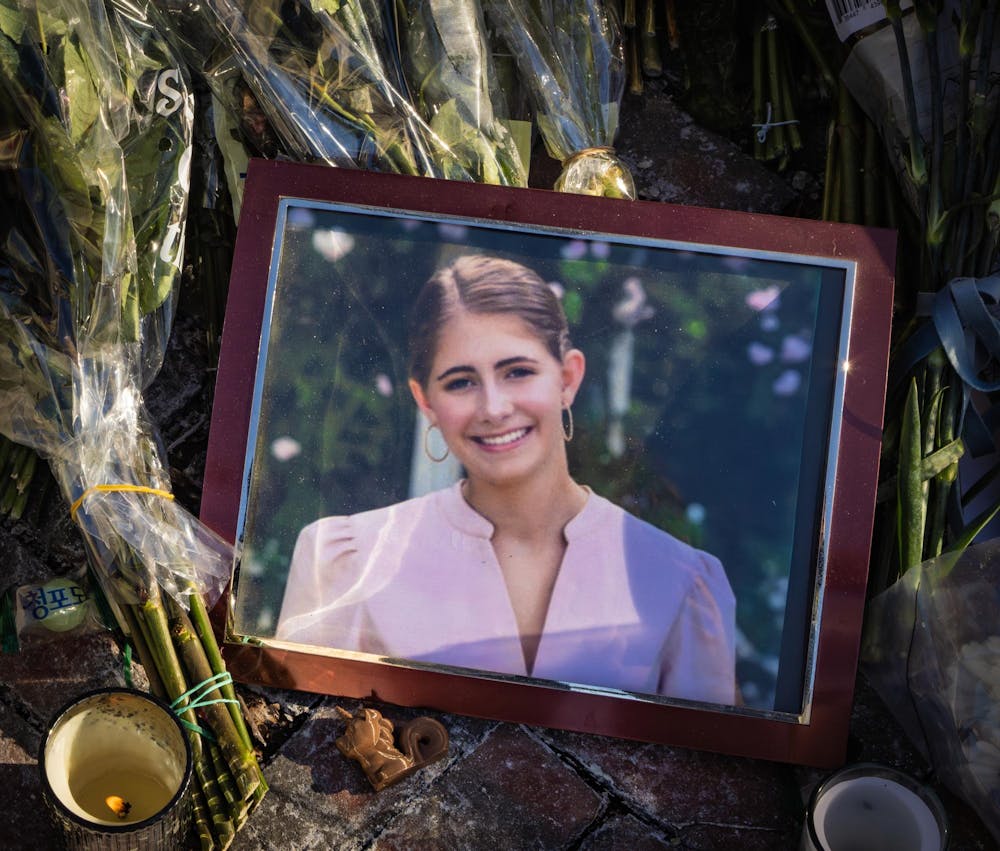 A picture frame of a smiling girl sits on top of bouquets of flowers. 