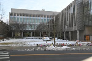 The Barus and Holley building, which is gray and multiple stories tall, with a silver infinity sign sculpture and flowers on the snowy ground in front of it. 