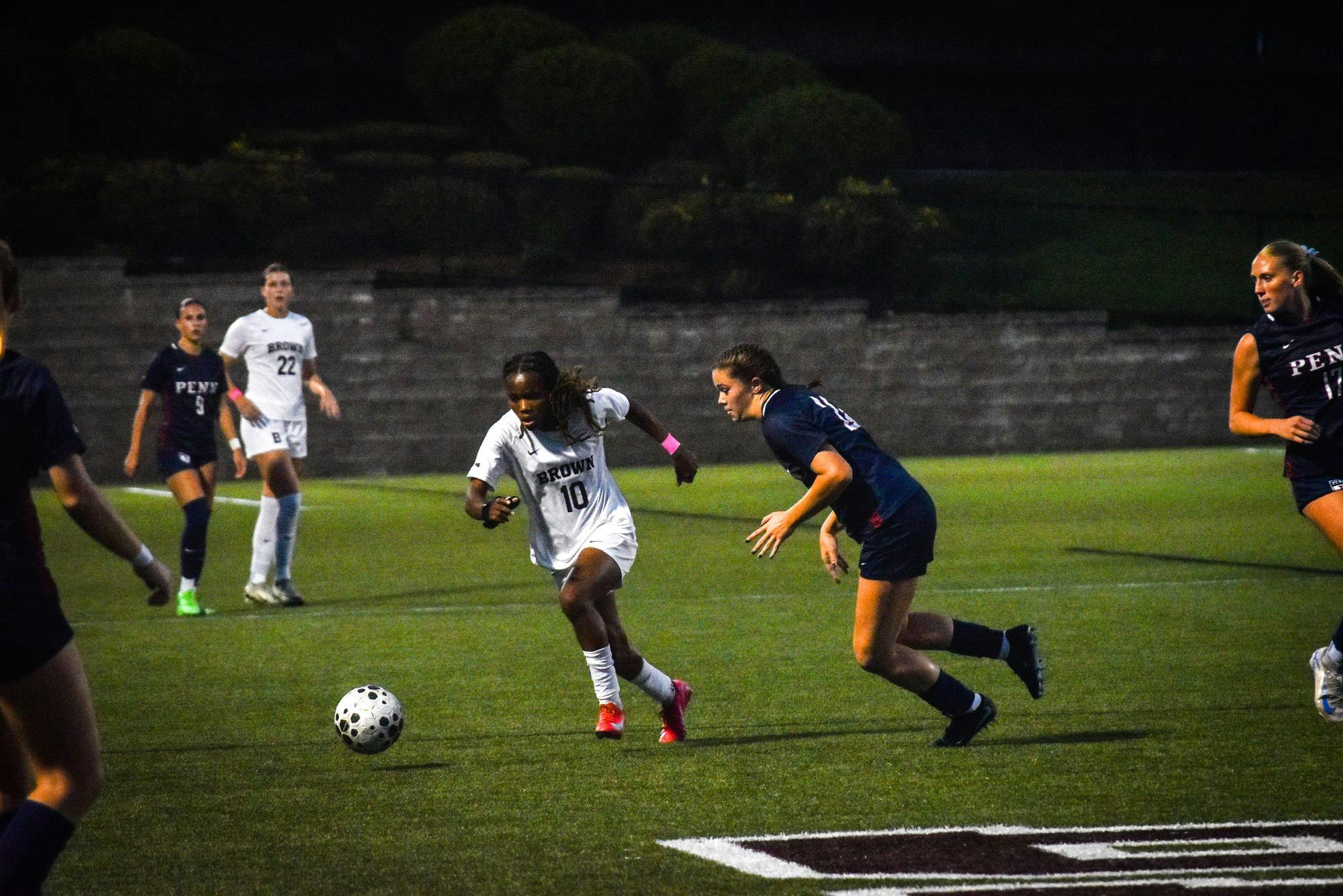 Photo of a soccer player wearing a white jersey sprinting towards a ball, followed closely by an opponent in blue. 