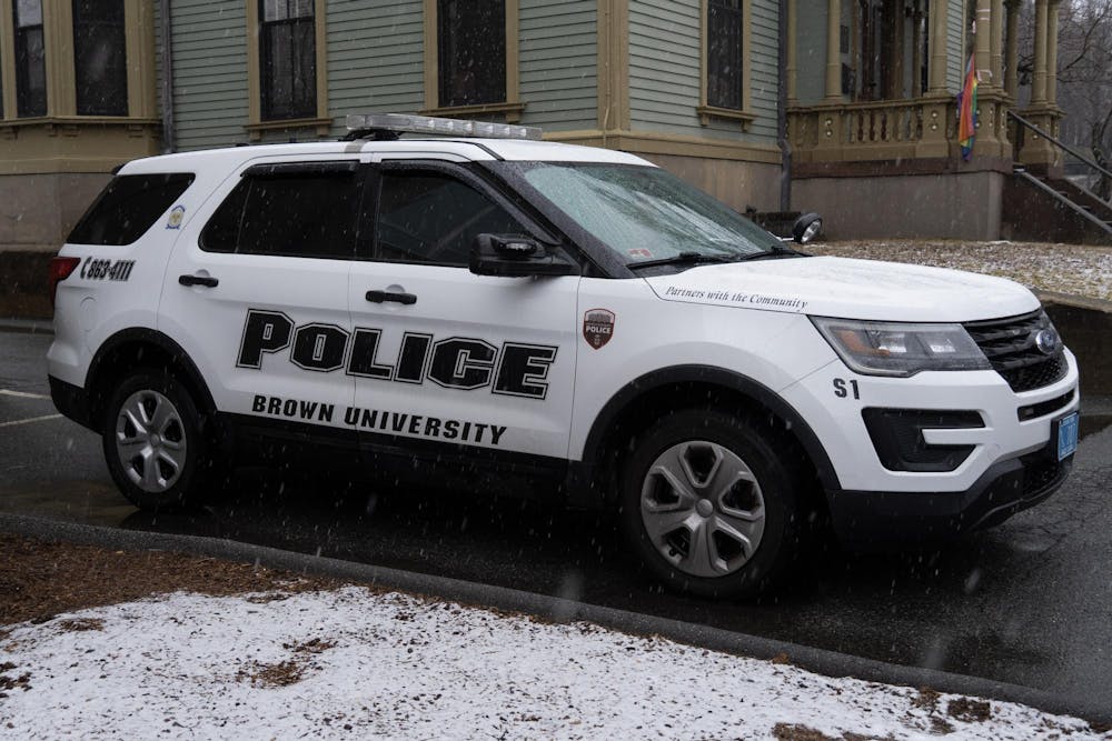 A photo of the side view of a Brown University police car parked on the street while it is snowing outside. 