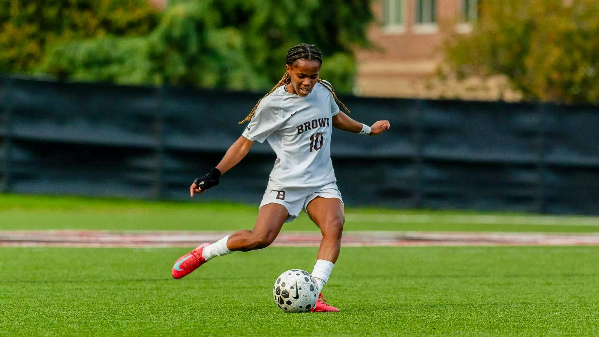 A Brown women's soccer player setting up to kick a ball.